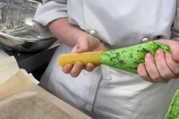 A hospitality student in a white chef's jacket pipes ricotta filling into cannelloni pasta in a professional kitchen