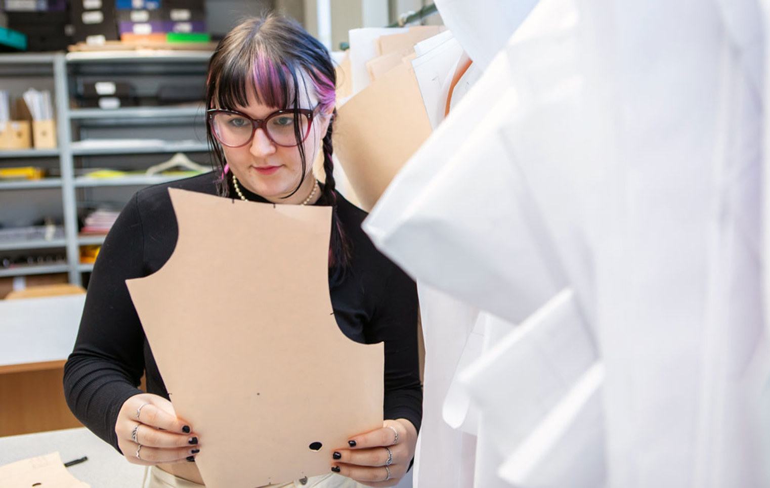 A fashion student examining a paper pattern for garment design in a sewing studio.