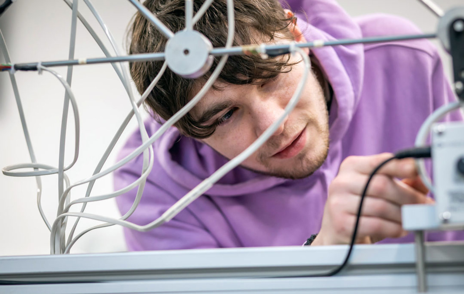 A student in a purple hoodie carefully adjusting wires on a mechanical assembly, focused on a hands-on engineering project.