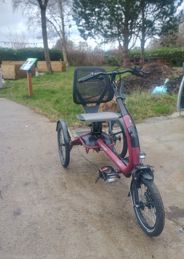 Three-wheeled adapted bike designed for accessible cycling, shown in an outdoor community garden setting.