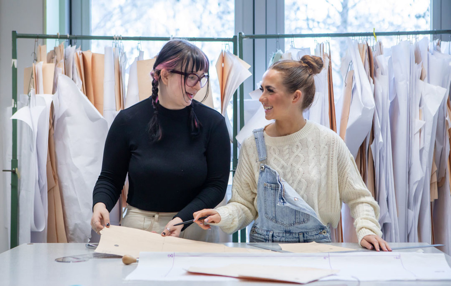Two fashion students laughing while working on design patterns in a classroom.