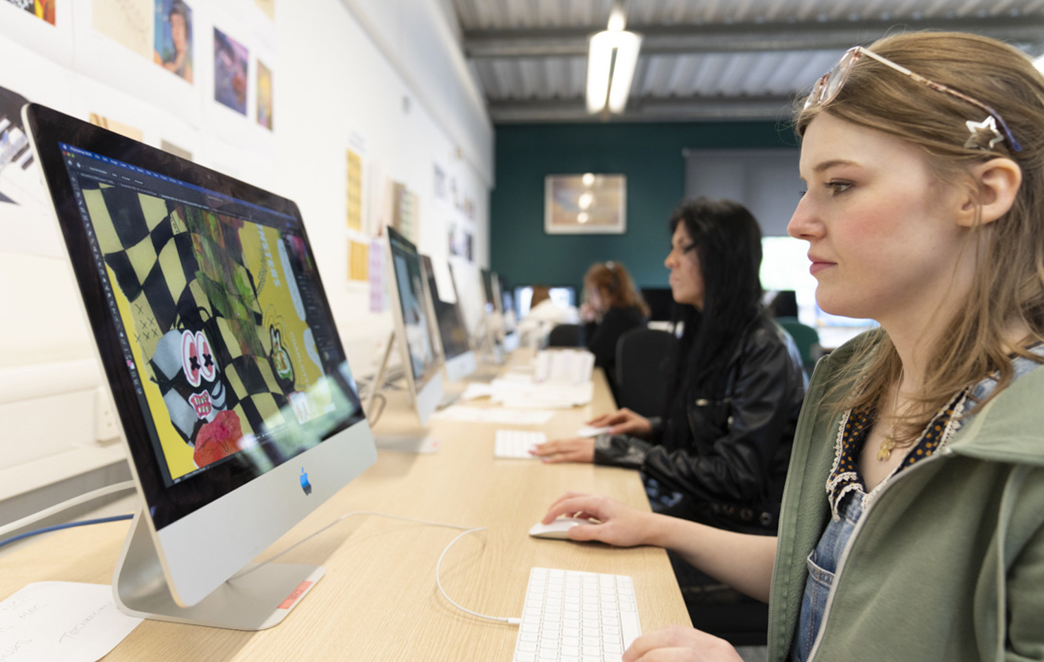 Student creating digital artwork on a desktop computer in a classroom with creative posters on the wall.
