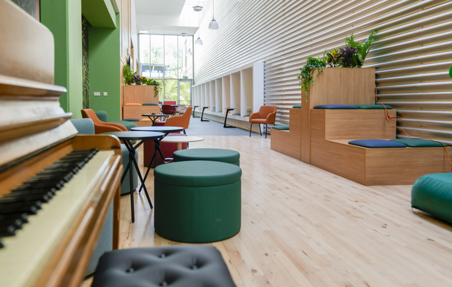 Stylish student lounge with circular stools, lush green sofas, and a mural of tropical plants.