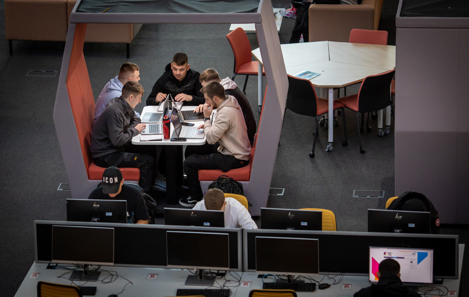 Group of male students working together on laptops in a study pod at Glasgow Kelvin College’s Springburn campus, with others using nearby desktop computers.