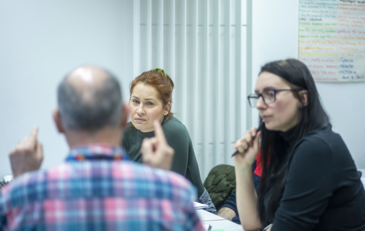 Lecturer leads a class discussion with students seated around a table and a population graph displayed behind.