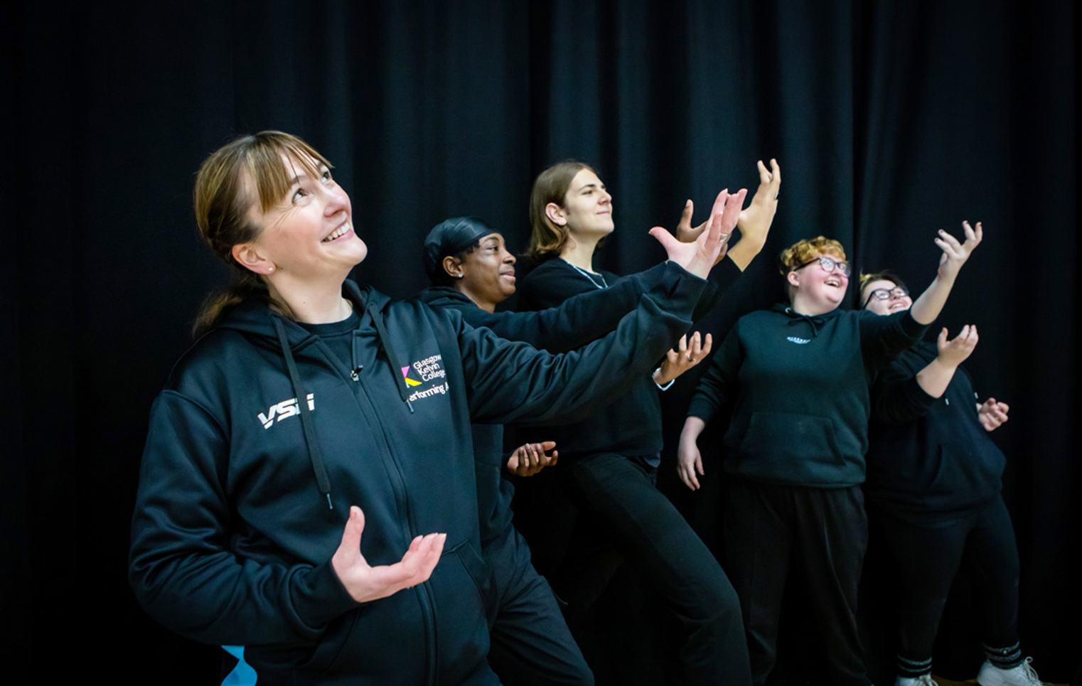 Performing arts lecturer leading a drama exercise with students, demonstrating expressive hand and body movements.