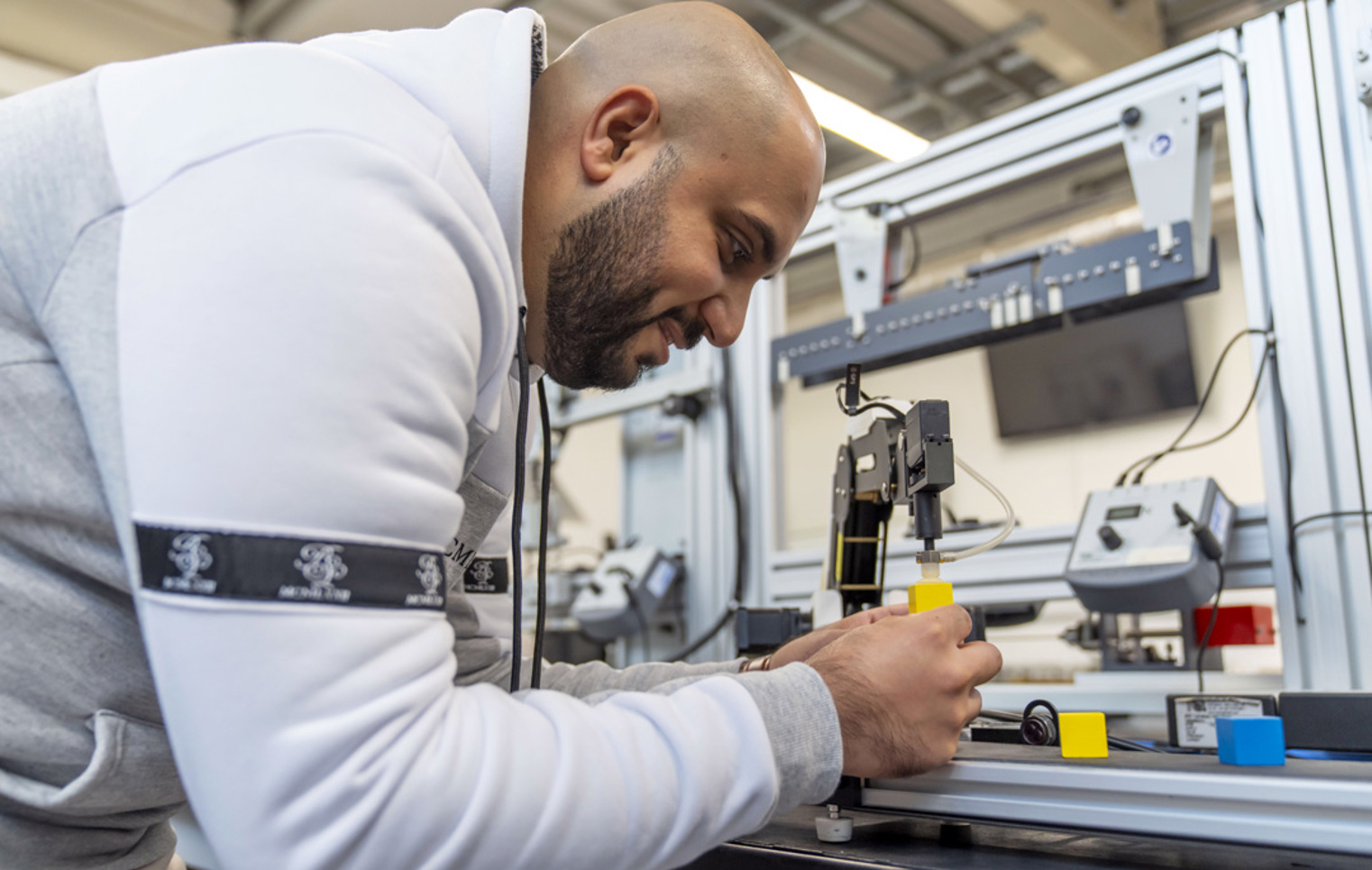 Student operating a robotic arm, carefully placing a yellow block on a conveyor system as part of an automation project
