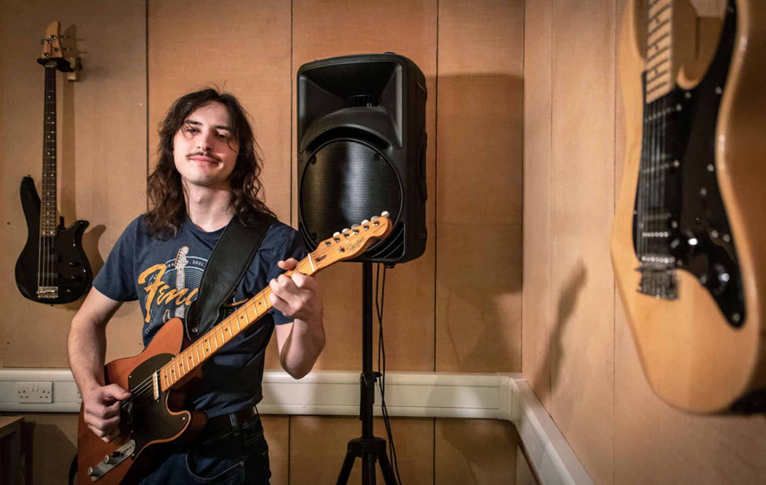 A guitarist wearing a Fender t-shirt playing an electric guitar.