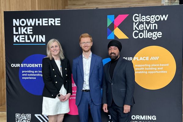 Visitors posing in front of Glasgow Kelvin College branding display during campus visit.