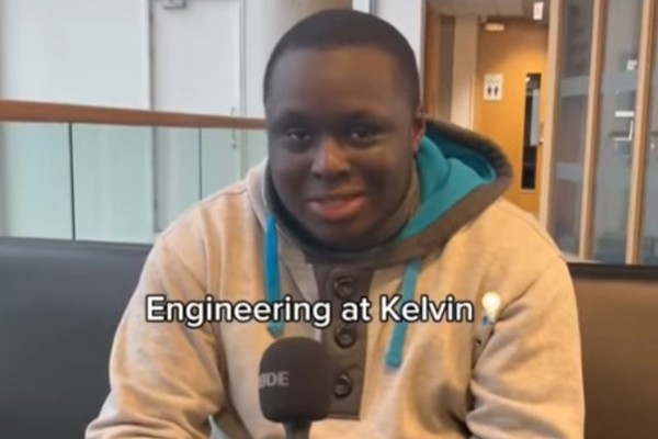 A student in a grey and teal hoodie sitting on a black sofa, holding a microphone and smiling. The text overlay reads 'Engineering at Kelvin 💡' with the student introducing themselves as studying HNC Mechanical Engineering at Glasgow Kelvin College.