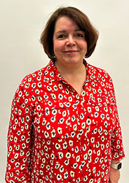 Moira MacDonald, wearing a red patterned blouse, smiles against a plain background