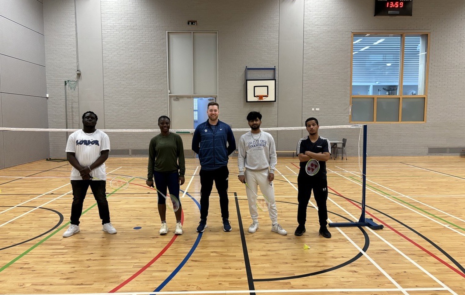 Group of students and a coach posing in the gym hall at Glasgow Kelvin College after a badminton session, standing on either side of the net.