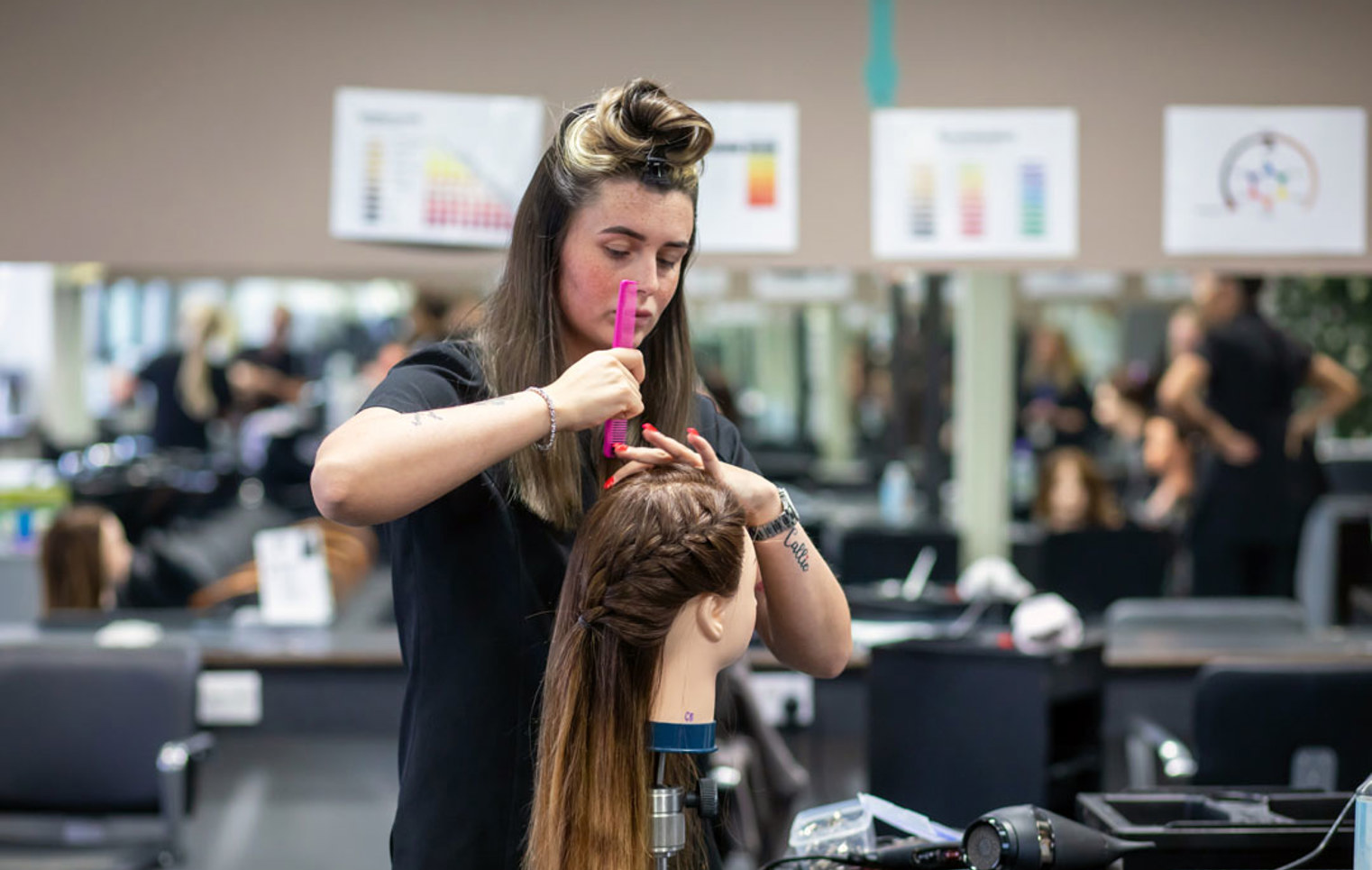 Hairstyling student carefully styling a mannequin’s hair in a salon.