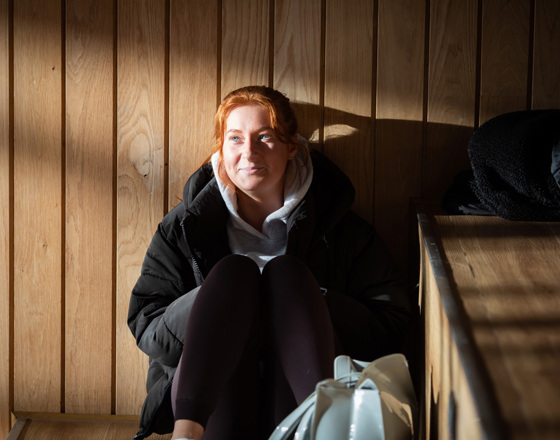 Student sitting in sunlight on wooden steps at Glasgow Kelvin College Springburn campus, wearing casual clothes and smiling softly