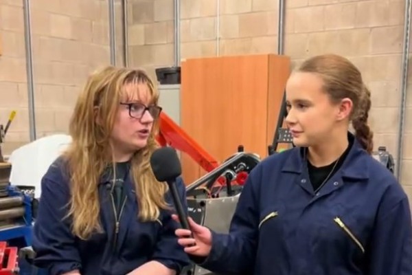 Automotive students in workshop overalls taking part in a filmed interview in a college engineering workshop.