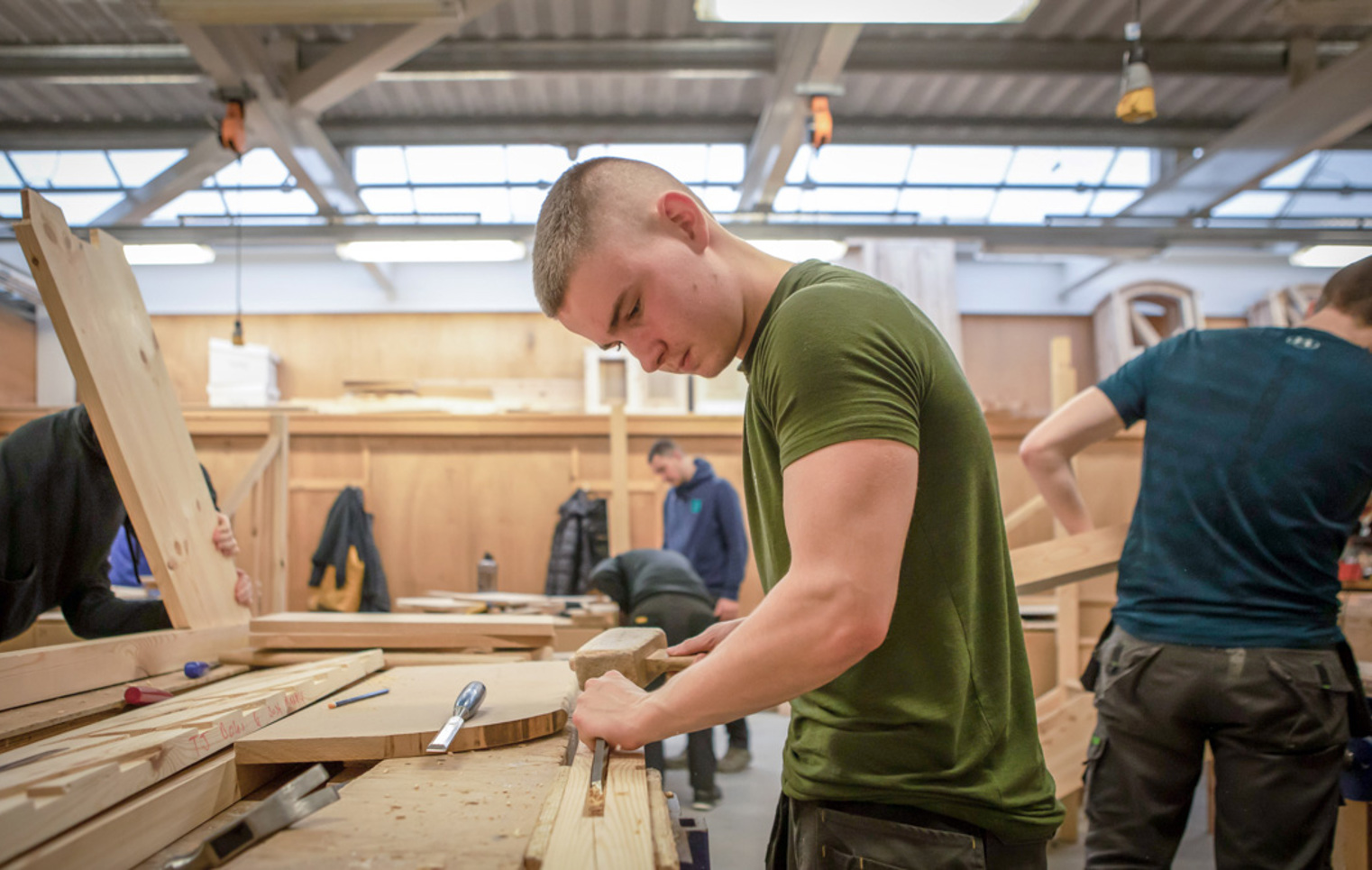 A joinery student focused on chiseling wood, using a mallet at a workbench during practical training in a woodworking class.