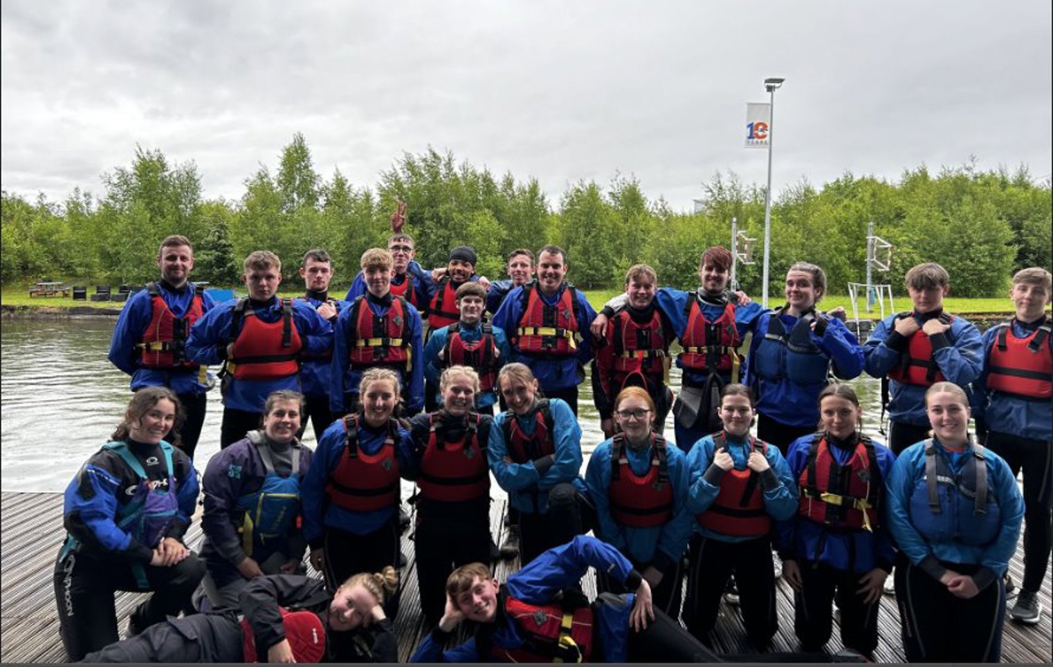  Group of Glasgow Kelvin College students wearing wetsuits and life jackets posing together at Pinkston Watersports Centre after an outdoor activity session.