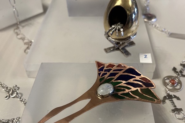 A selection of handcrafted jewellery on display at Craftex 2025, featuring a copper bowl, sculpted egg piece, and an enamelled decorative hairpin.