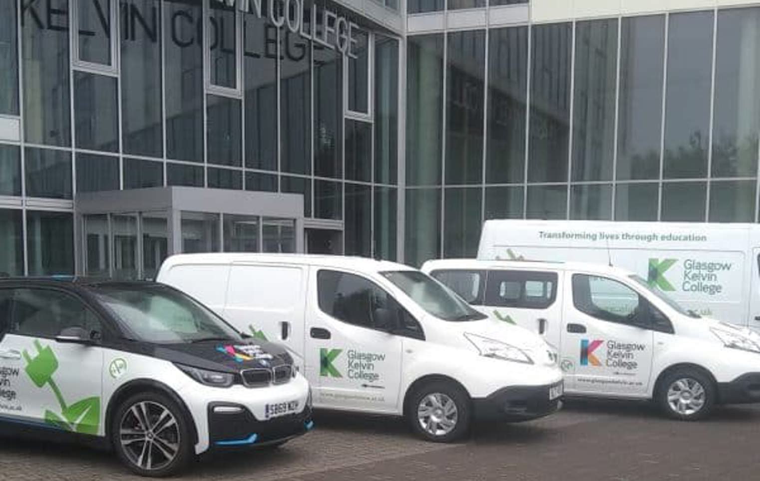 Fleet of electric vehicles branded with Glasgow Kelvin College logos parked outside the college's modern glass-fronted building.