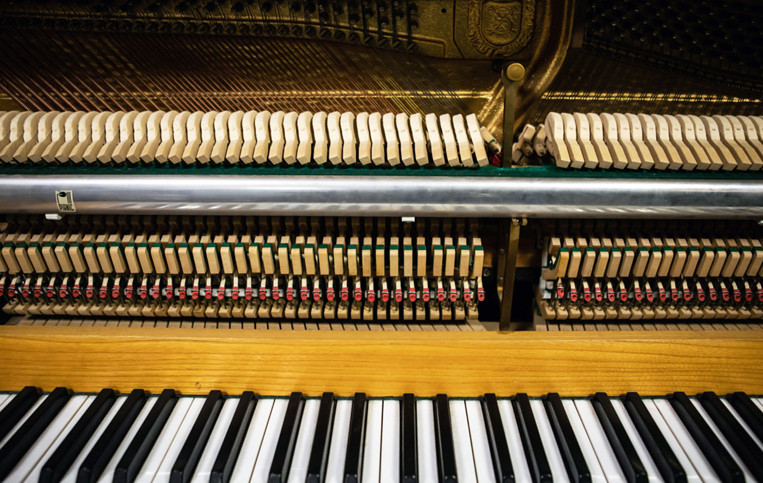 A close-up view of an upright piano’s inner mechanics, showing hammers, strings, and the keyboard.