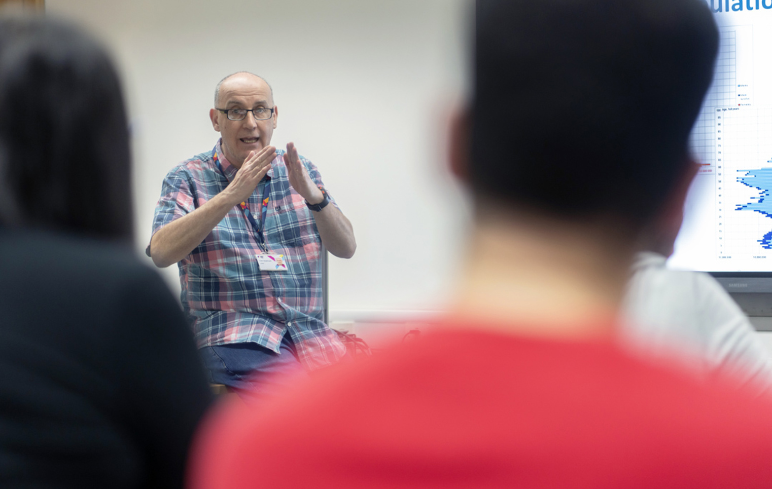 Lecturer uses hand gestures while explaining a topic to students in a humanities lesson.