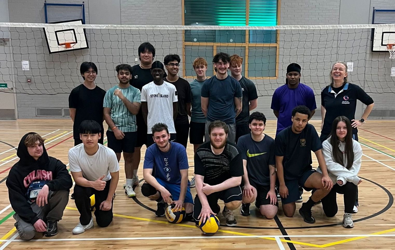 Glasgow Kelvin College students posing as a volleyball team in the sports hall, standing and kneeling in front of the net.
