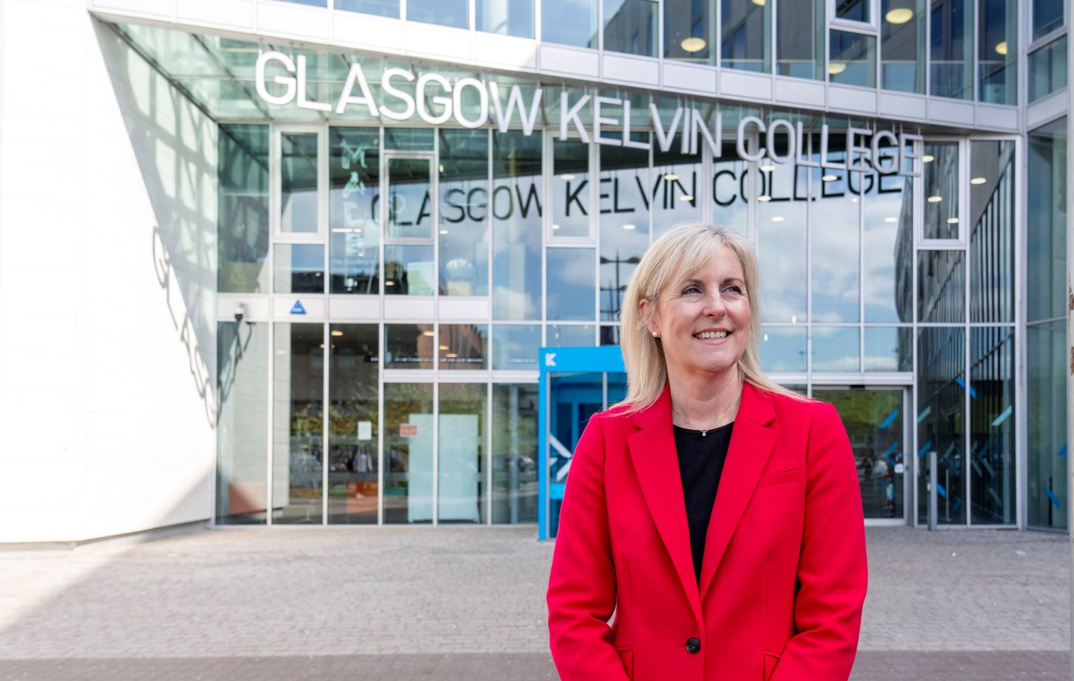 Joanna Campbell, Principal of Glasgow Kelvin College, smiling outside the college’s main entrance in a bright red blazer