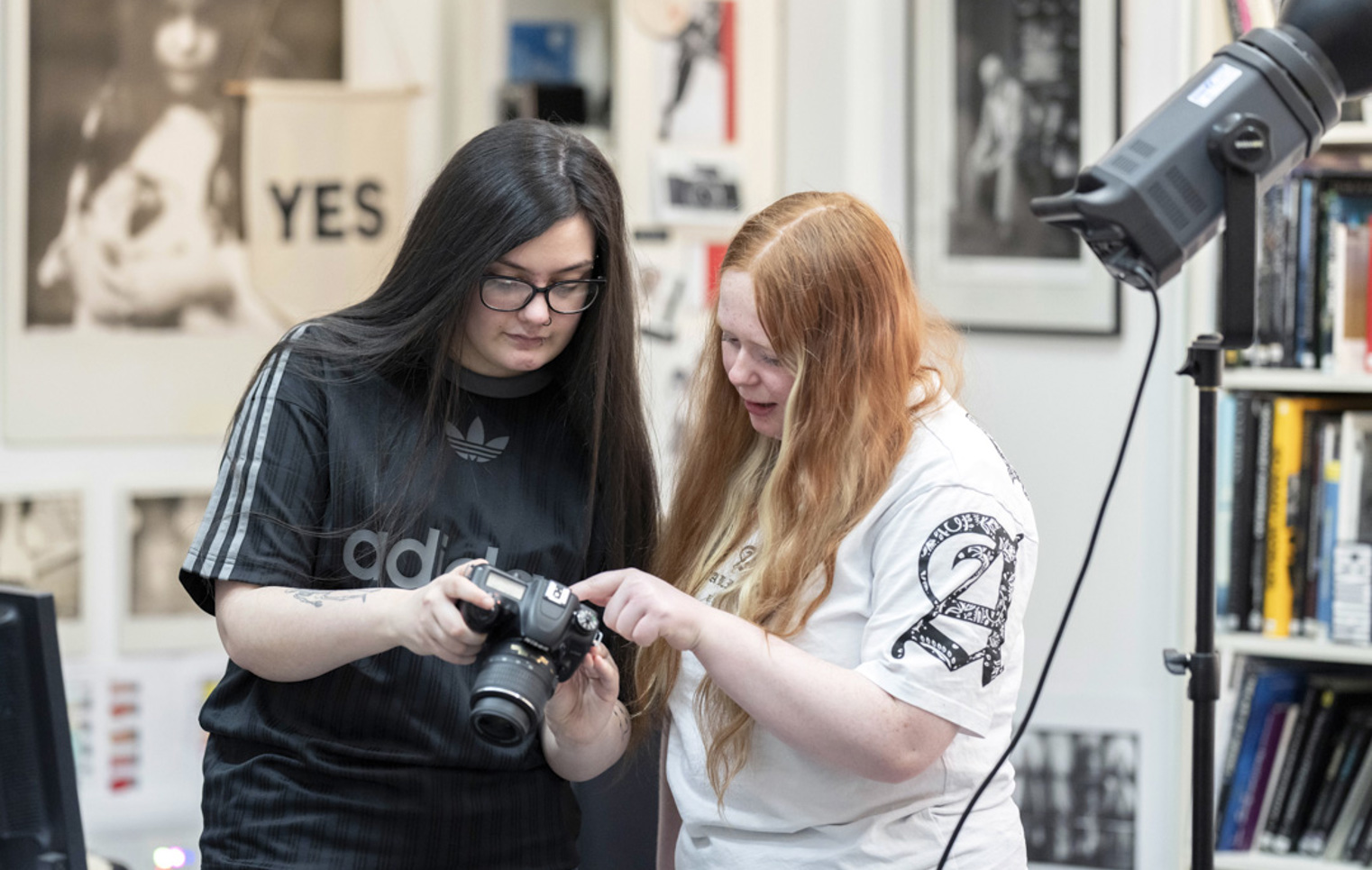 Two students reviewing photos on a DSLR camera in a creative photography studio.