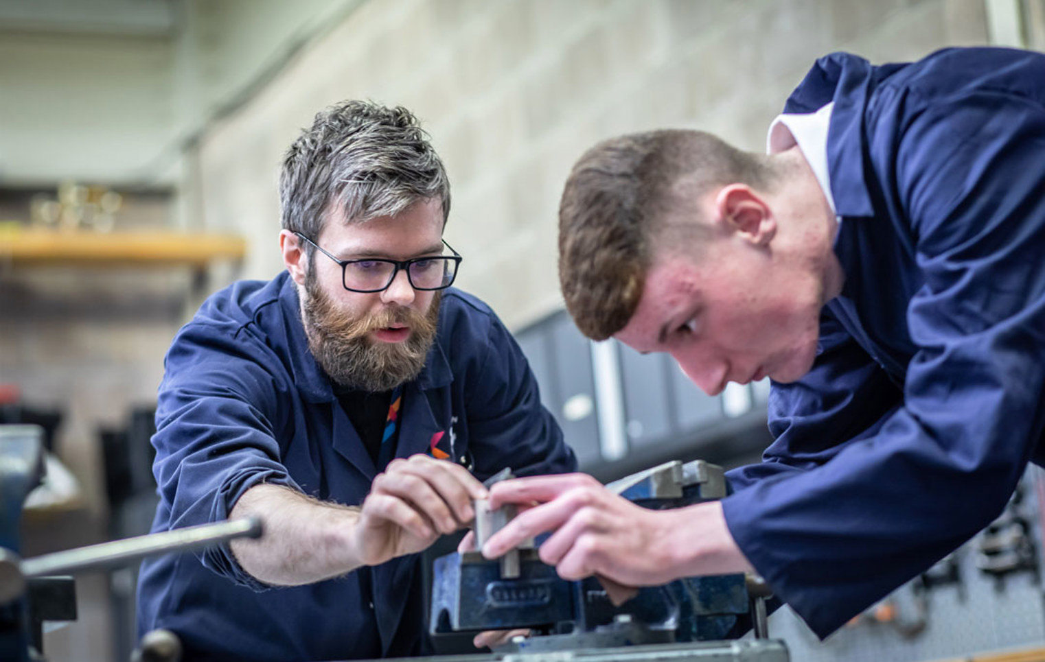 Lecturer and student working together on precision metalwork using workshop equipment.