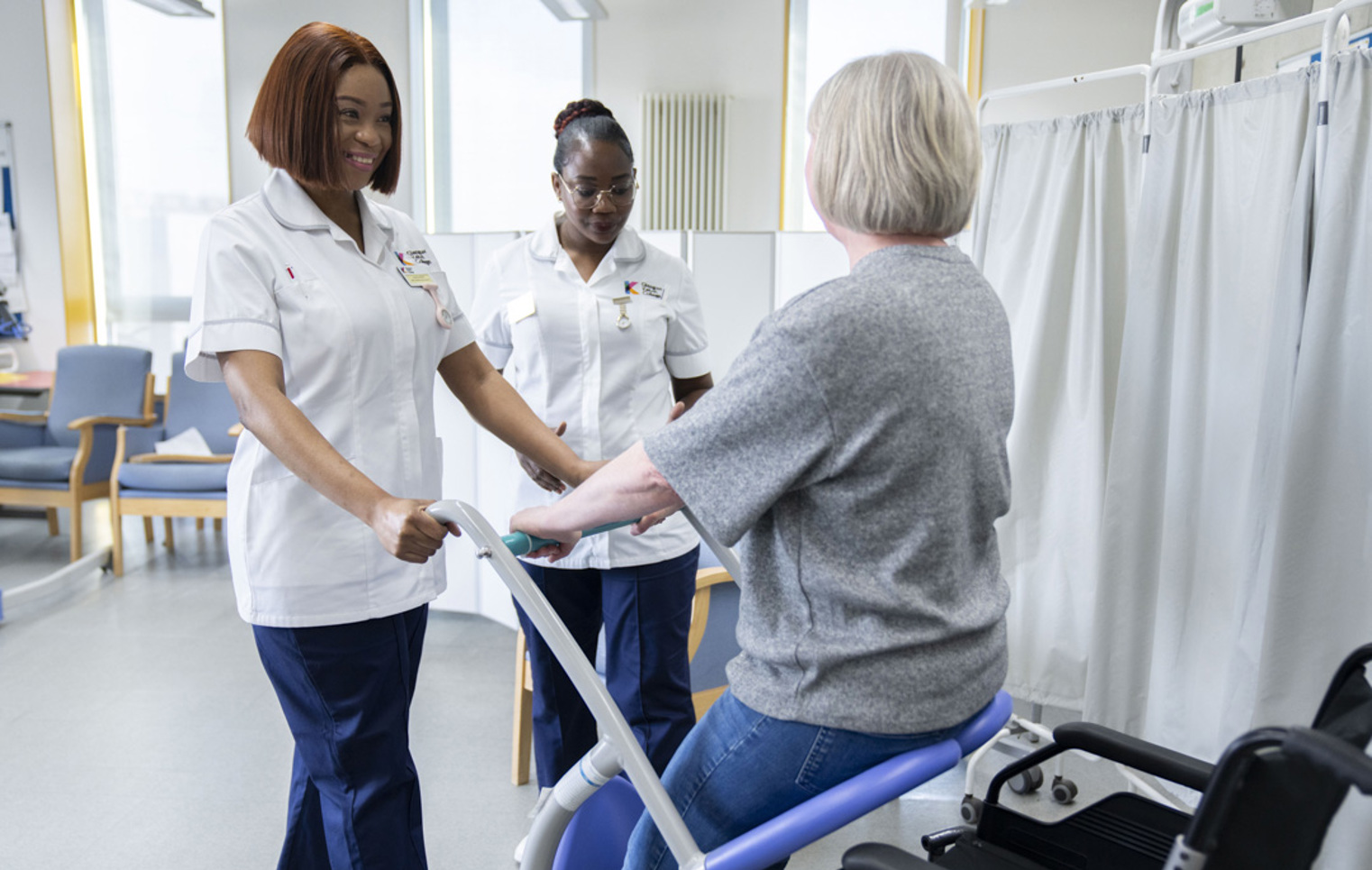 Two healthcare students assist a patient using a mobility aid in a simulated care environment.