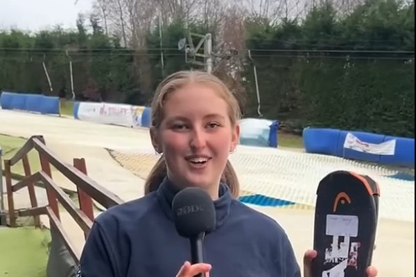 Outdoor Adventure Sports student Sarah speaking into a microphone while holding skis at an outdoor ski slope.