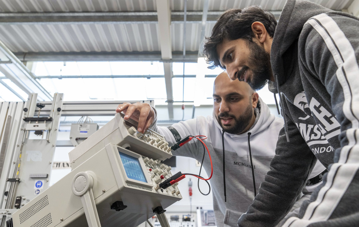 Two students working together on an oscilloscope, adjusting settings to analyze waveforms in an electronics engineering lab.
