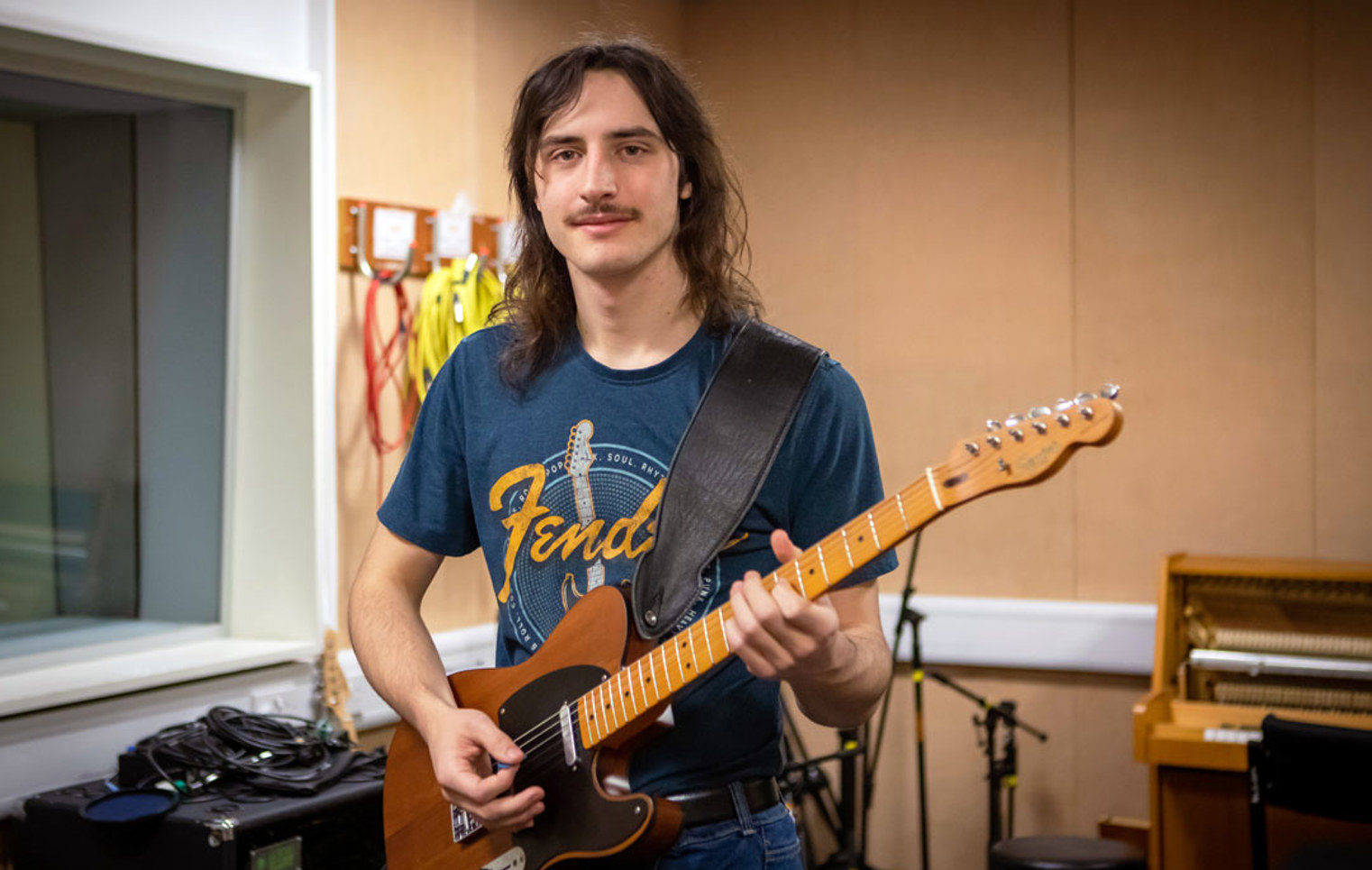 A guitarist smiling while playing a Fender Telecaster in a practice room.