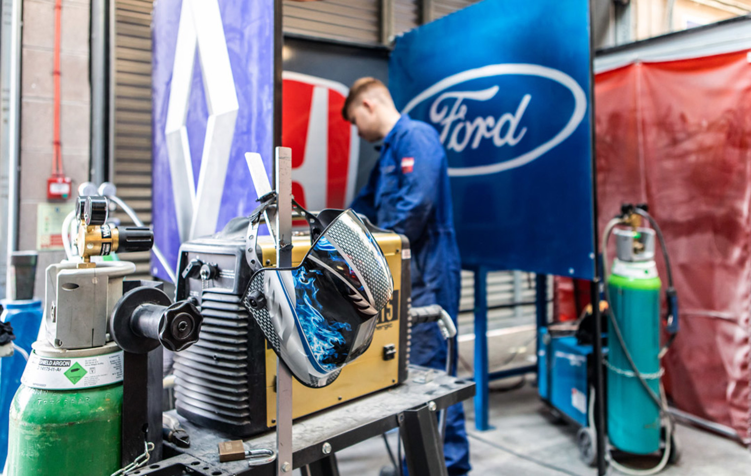 Close-up of automotive welding area showing gas cylinders and a protective welding mask.