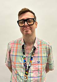 Portrait of Jon Craig wearing a colourful checked shirt, black glasses, and a Glasgow Kelvin College lanyard, standing against a plain background.