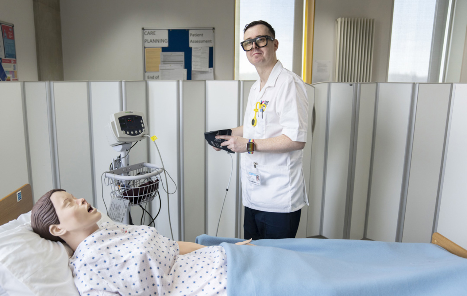 Student prepares to check vital signs on a training mannequin in a simulated hospital ward.