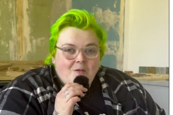 A Photography student at Glasgow Kelvin College with bright green hair and tattoos speaks into a microphone, discussing architecture photography during an interview.