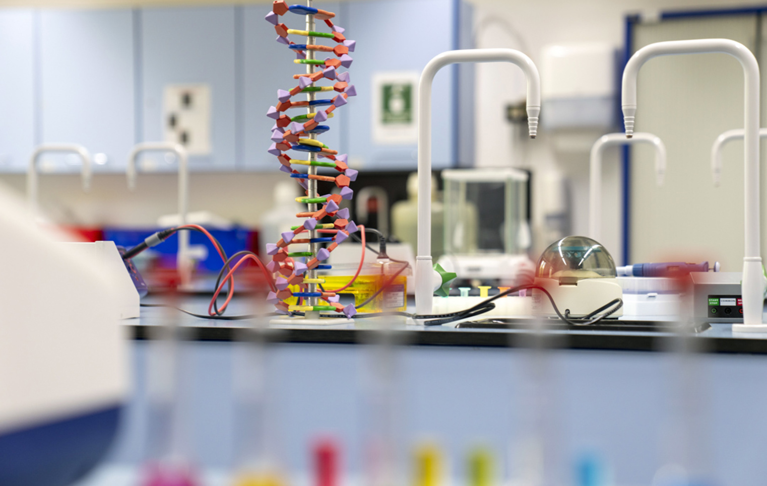 A colourful DNA model stands tall in the middle of a bright science lab bench, surrounded by equipment and science gadgets—ready for some creative experiments and discovery