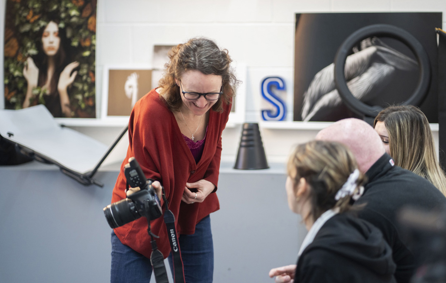 Lecturer smiling and giving feedback to photography students reviewing images on a DSLR camera.