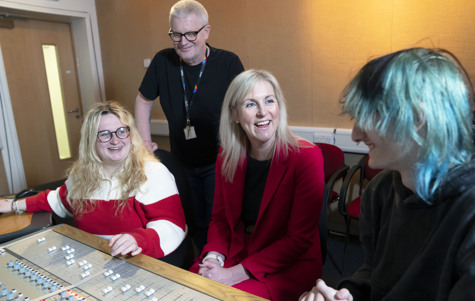Principal Joanna Campbell chats with students and a staff member in a Glasgow Kelvin College recording studio, all smiling around a sound mixing desk.