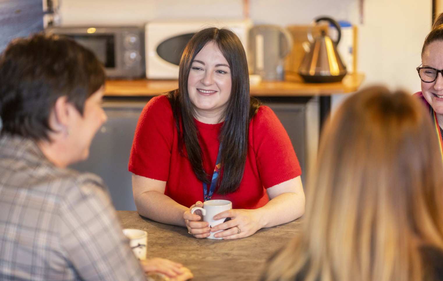 Support staff at Glasgow Kelvin College enjoying a relaxed conversation over coffee in a staff kitchen area.