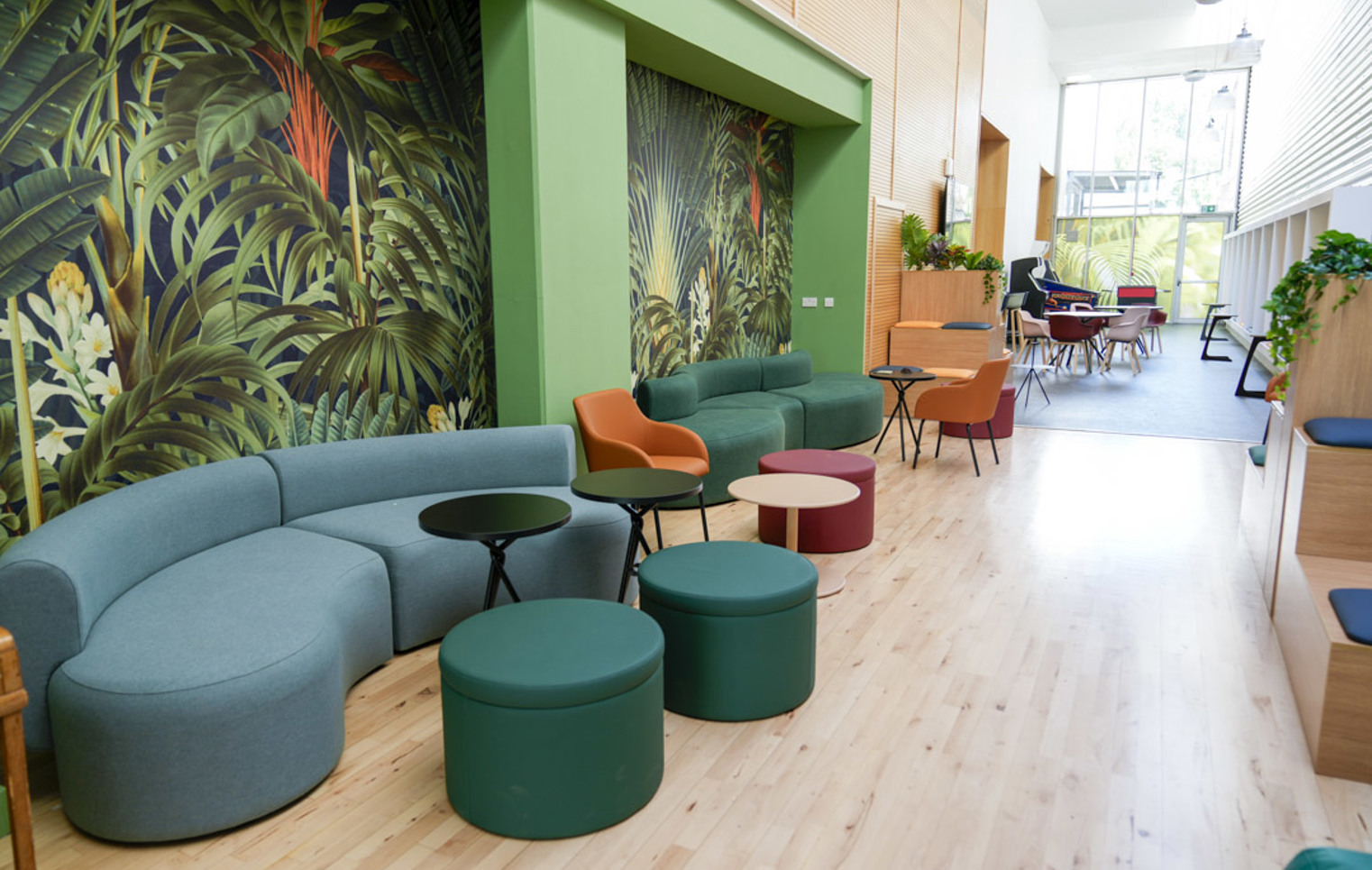 Seating area with green and orange cushioned benches, black side tables, and colourful wallpaper in a student hub.