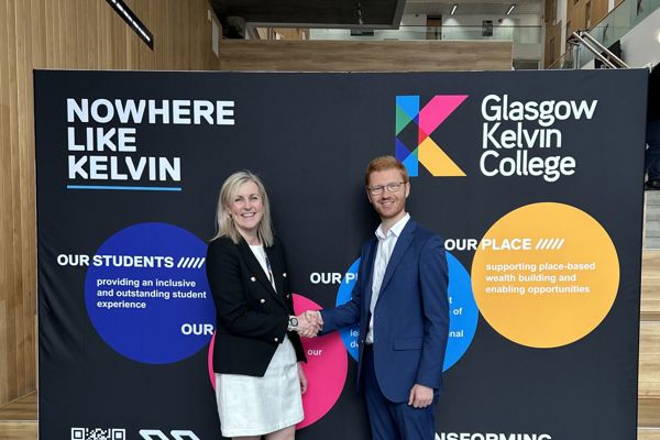 Handshake between Glasgow Kelvin College representative and visiting partner in front of college branding display.
