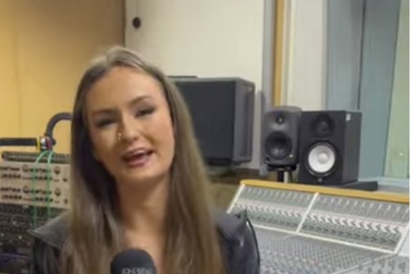 Caitlyn Sharp, a student on the Music Business course at Glasgow Kelvin College, speaks into a microphone in a recording studio, seated in front of a mixing desk.