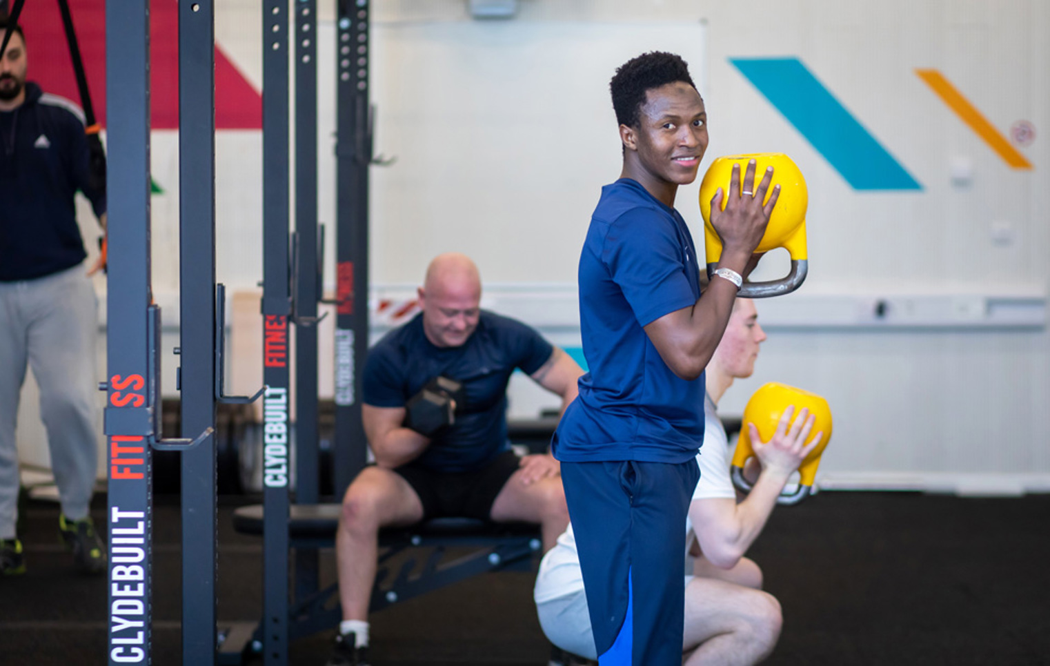 Student smiling while holding a yellow kettlebell during a strength training session at the gym.