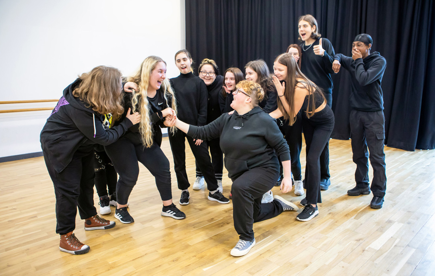 Performing arts students gathered in a studio rehearsal, reacting enthusiastically during a group improvisation exercise.