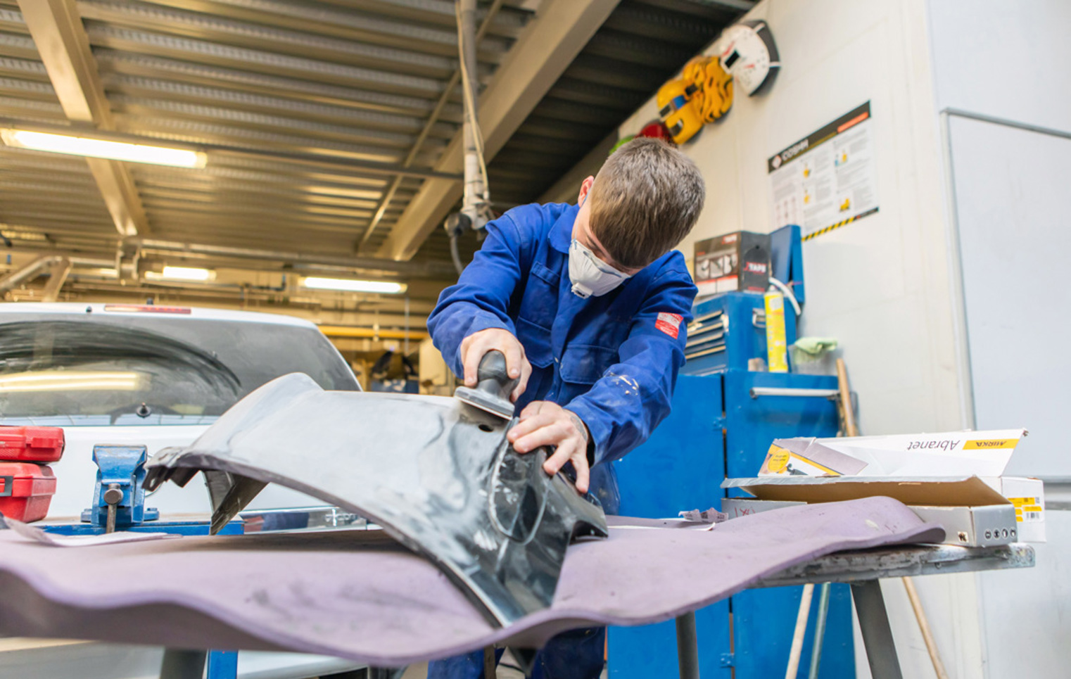Student in blue overalls sanding a car panel in the Glasgow Kelvin College automotive workshop.