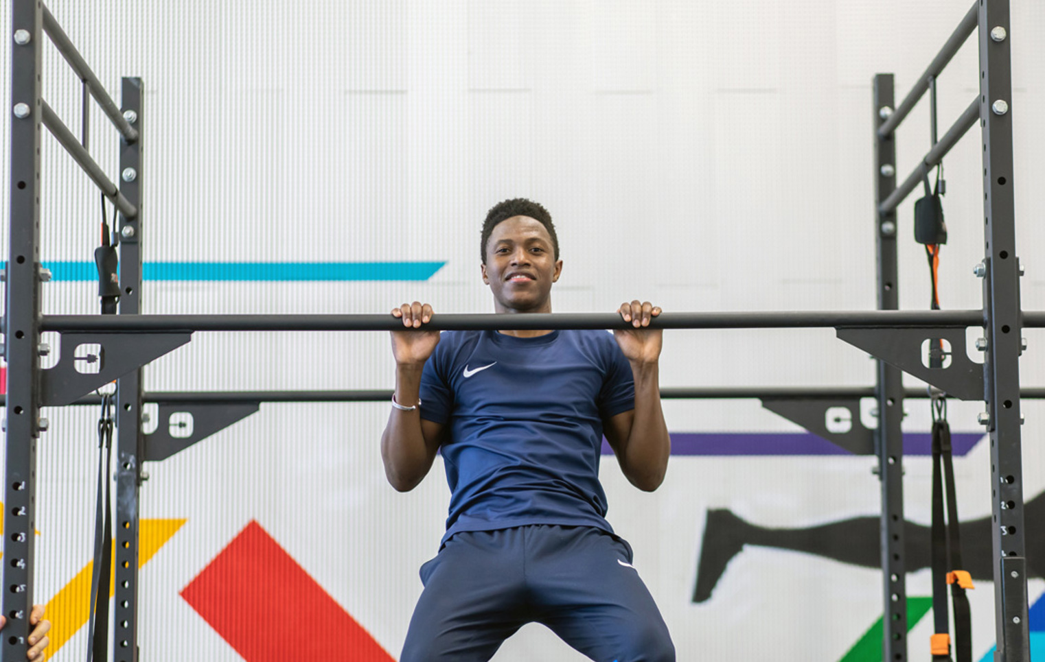 Student mid-pull-up on gym rig with colourful wall graphics behind.
