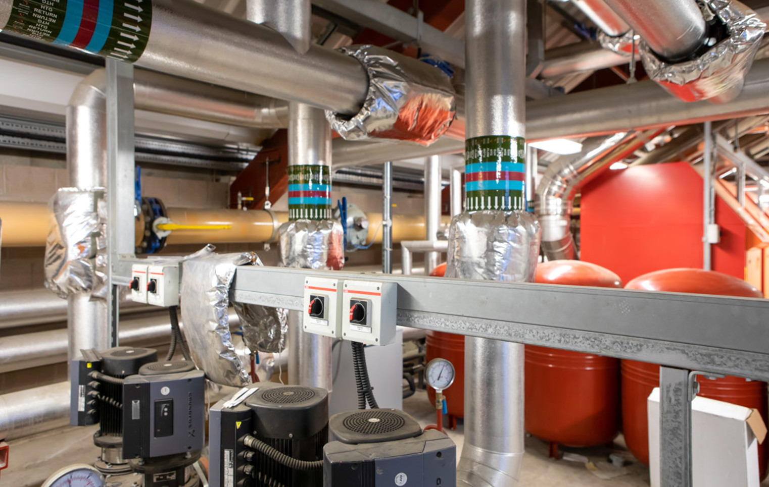 Close-up of interconnected heating system pipes, pumps, and insulated valves used for industrial heating and ventilation.