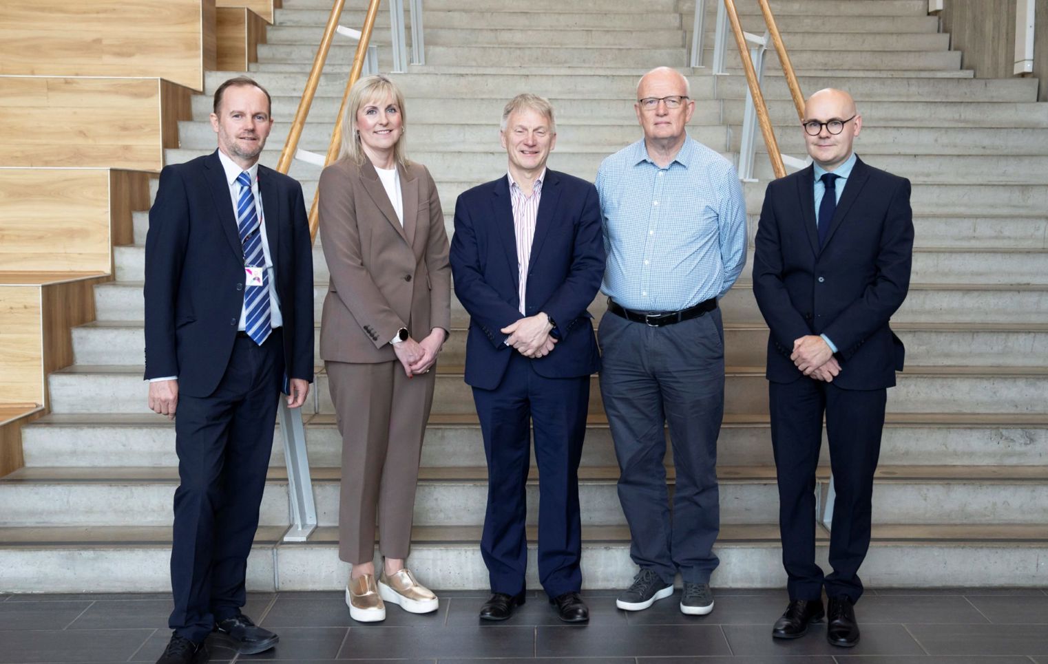 Five professionally dressed individuals standing on indoor stairs at Glasgow Kelvin College.